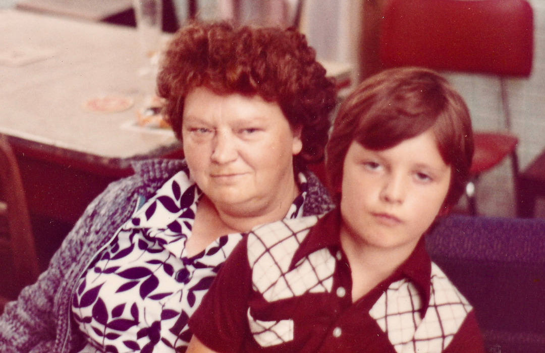 Five-year-old boy Alex Nelles sits on his grandmother’s lap. The image marks the beginning of his journey, where he learned that he wanted to make others’ lives easier through digital transformation. Both calmly gaze into the camera while sitting in a homely environment.